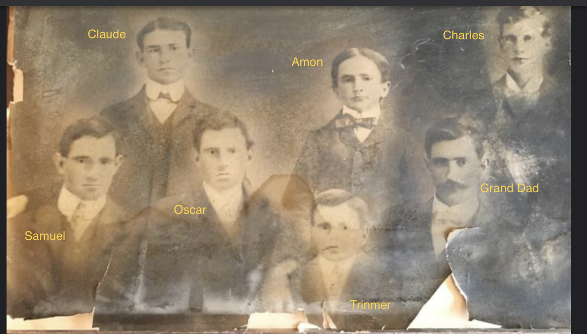 Black and white vintage photograph featuring seven men, labeled with names: Claude, Charles, Amon, Oscar, Samuel, Grand Dad, and Trinmer, capturing a historical moment from the past.
